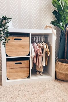 a white cabinet with drawers and clothes hanging on the wall next to a potted plant