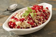 a white bowl filled with rice and pomegranates next to a spoon