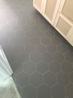 a bathroom with gray hexagonal tiles on the floor and cabinets in the background