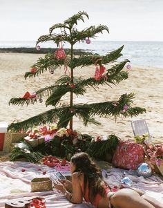 a woman laying on the beach next to a christmas tree