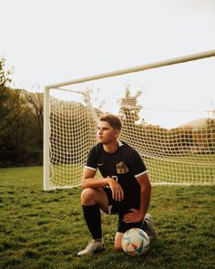 a man sitting on the ground next to a soccer ball in front of a goal