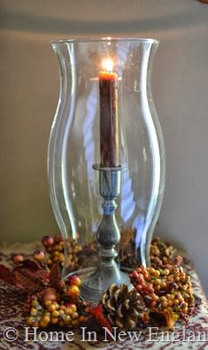 a candle is lit in a glass vase filled with pine cones and other autumn decorations