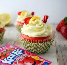 some cupcakes with white frosting and strawberries on top are sitting on a table