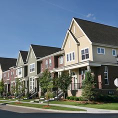 a row of townhouses with trees and bushes on the side of the street in front of them