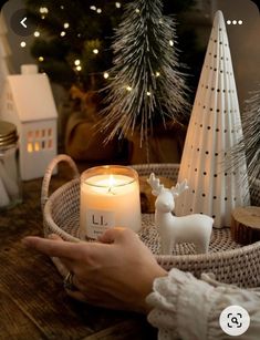 a person holding a lit candle in front of a christmas tree and other decorations on a table