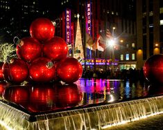 a fountain with christmas ornaments on top and lights reflecting off the water in front of it