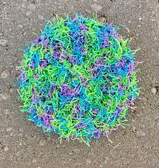 a blue and green ball on the ground with grass sprinkled all over it