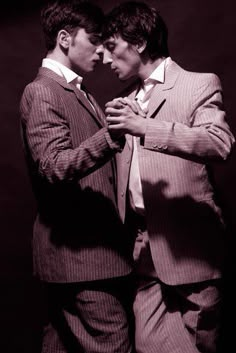 two men in suits standing next to each other with their hands on their chests