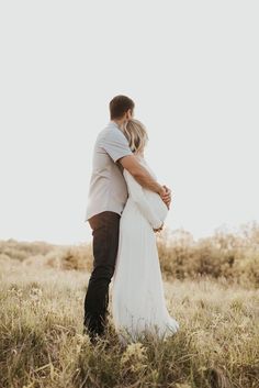 a man and woman standing in the middle of a field with their arms around each other