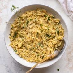 a white bowl filled with pasta and parsley on top of a marble countertop