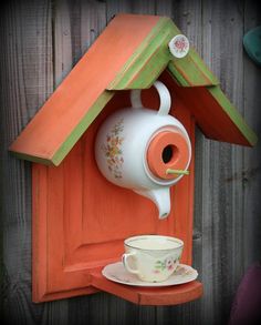 an orange birdhouse with a tea cup and saucer on it's side