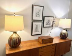 two lamps are sitting on top of a wooden dresser next to pictures and a lamp shade