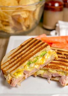 a sandwich cut in half sitting on top of a white plate next to watermelon and potato chips