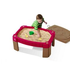 a little boy playing in a sandbox with toys on it's sides and an open lid