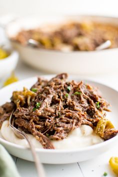 a white bowl filled with food next to another bowl full of meat and potatoes on a table