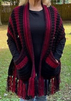 a woman standing in the grass wearing a red and black crocheted cardigan