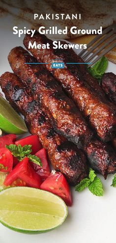 grilled meat skewers on a white plate with limes and tomatoes