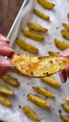 someone holding up a piece of food in front of some potatoes on a baking sheet