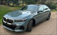 a blue bmw is parked in front of some trees