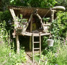 a tree house made out of branches in the middle of some plants and flowers around it