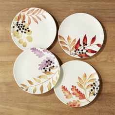 three plates with painted leaves on them sitting on a wooden table next to each other