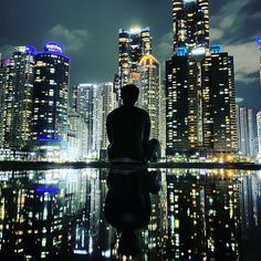 a man sitting on the edge of a body of water in front of tall buildings