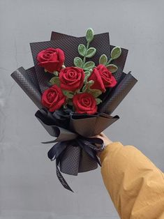 a hand holding a bouquet of red roses with green leaves and ribbons on it's side