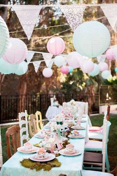 a table set up for a tea party with pink and white paper lanterns hanging from the ceiling