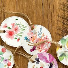 four handmade tags with watercolor flowers on them hanging from twine against a wooden surface