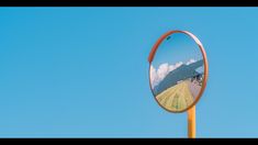 a round mirror on a wooden pole in front of a blue sky