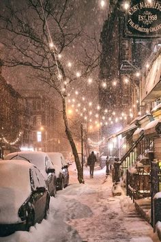 a city street covered in snow with cars parked on the side and people walking down the sidewalk