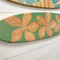 two surfboards with flowers painted on them hang from the wall next to each other