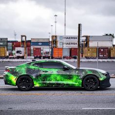 a green sports car is parked in front of some shipping containers on the side of the road