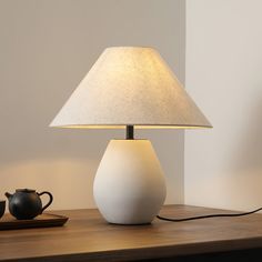 a table lamp sitting on top of a wooden table next to a teapot and cup