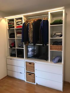 a white closet with drawers and clothes on it's shelves, all lit up by lights