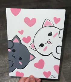 a hand holding up a small card with two cats on it and hearts in the background