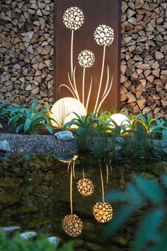 a pond surrounded by rocks and plants next to a wooden wall with flowers on it