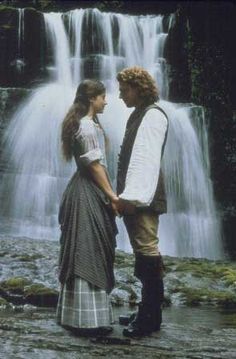 a man and woman standing in front of a waterfall