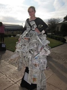 a woman in a newspaper dress is standing on the sidewalk with her arms around her waist