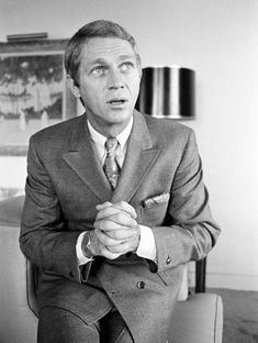 a man in a suit and tie sitting on a chair with his hands folded up