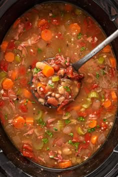 a spoon full of soup in a crock pot with carrots, celery and beans