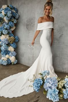 a woman in a white wedding dress standing next to blue and white hydrangeas