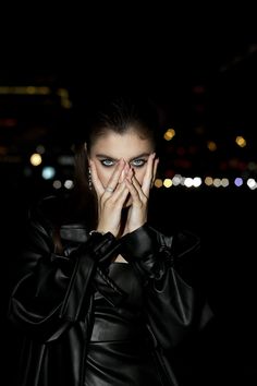 a woman covers her face with her hands while standing in front of the city lights