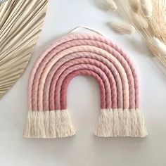 a pink and white wall hanging with tassels in the shape of a rainbow