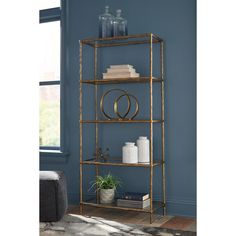 a gold metal shelf with books, vases and other items on it in front of a blue wall