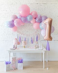 a birthday party with balloons, streamers and decorations on a table in front of a white brick wall