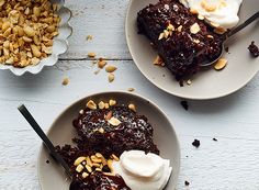 two white plates topped with desserts next to another plate filled with cake and nuts