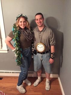 a man and woman standing next to each other in front of a wall with a clock on it