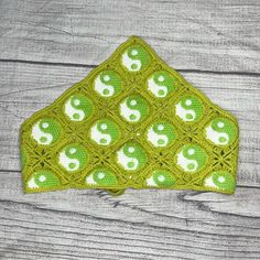 a crocheted green and white triangle with yin yang symbols on it, sitting on a wooden surface