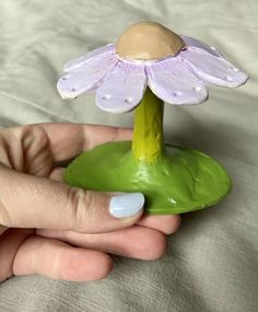 a hand holding a small purple flower on top of a green base